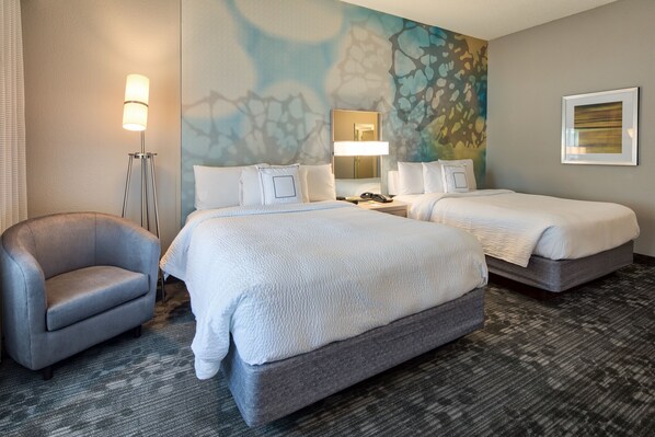 A hotel room with two beds, a chair, a desk, and a lamp.