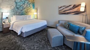 Een hotelkamer met een bed, een slaapbank, een nachtkastje, een lamp en een schilderij aan de muur.