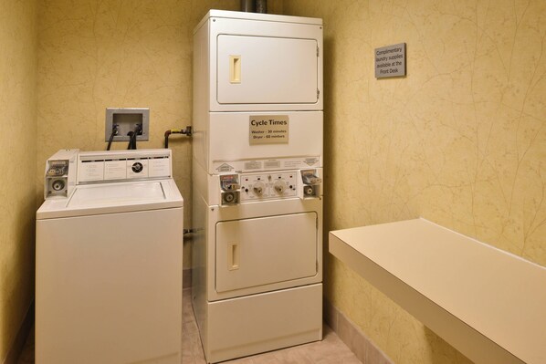 A laundry room with a front-loading washer and a stacked dryer. A sign indicates cycle times for the washer and dryer.