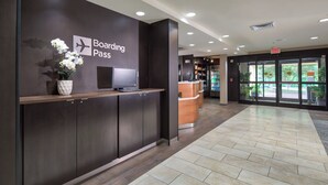 Een moderne receptie met een bord waarop 'Boarding Pass' staat, een receptiebalie en uitzicht naar buiten door glazen deuren.