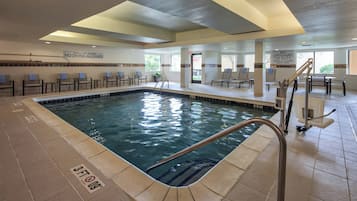 An indoor swimming pool with clear signage, a lifeguard station, and lounge chairs.