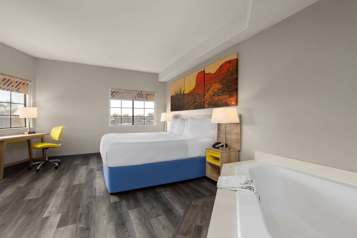 Una habitación de hotel moderna con cama, escritorio, silla y un ventanal grande.