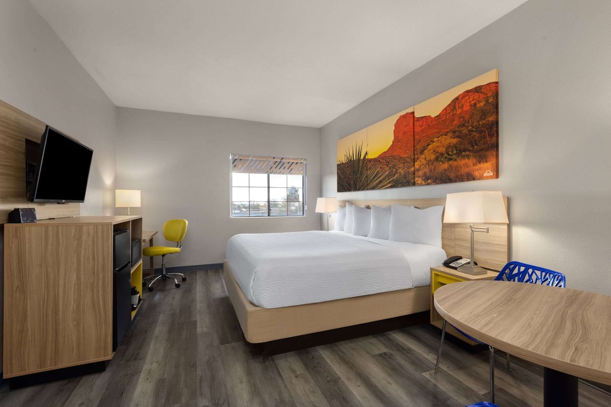 Una habitación de hotel con cama, escritorio, silla y un cuadro en la pared.