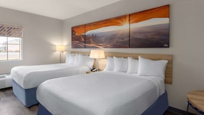 Habitación de hotel con dos camas, un cuadro grande de una puesta de sol, una lámpara y una mesita.