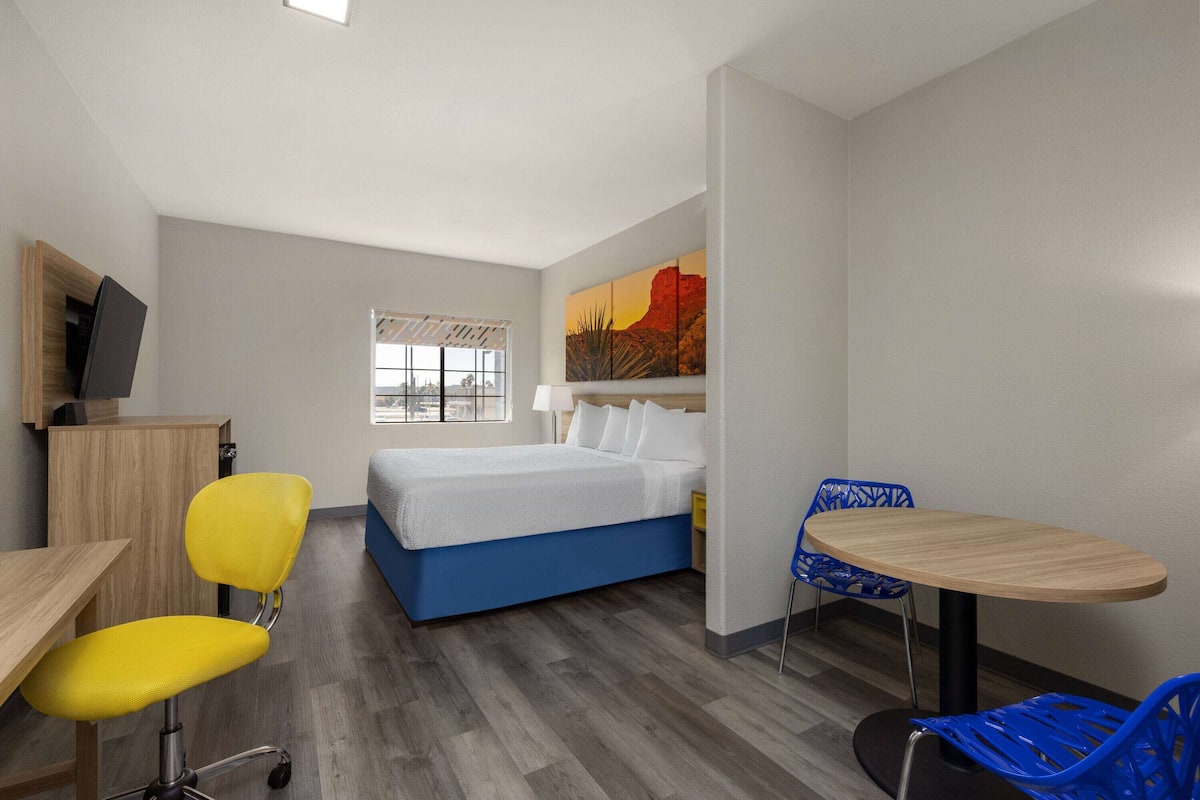Una habitación de hotel moderna con una cama, un escritorio, una silla, una mesa y un cuadro en la pared.