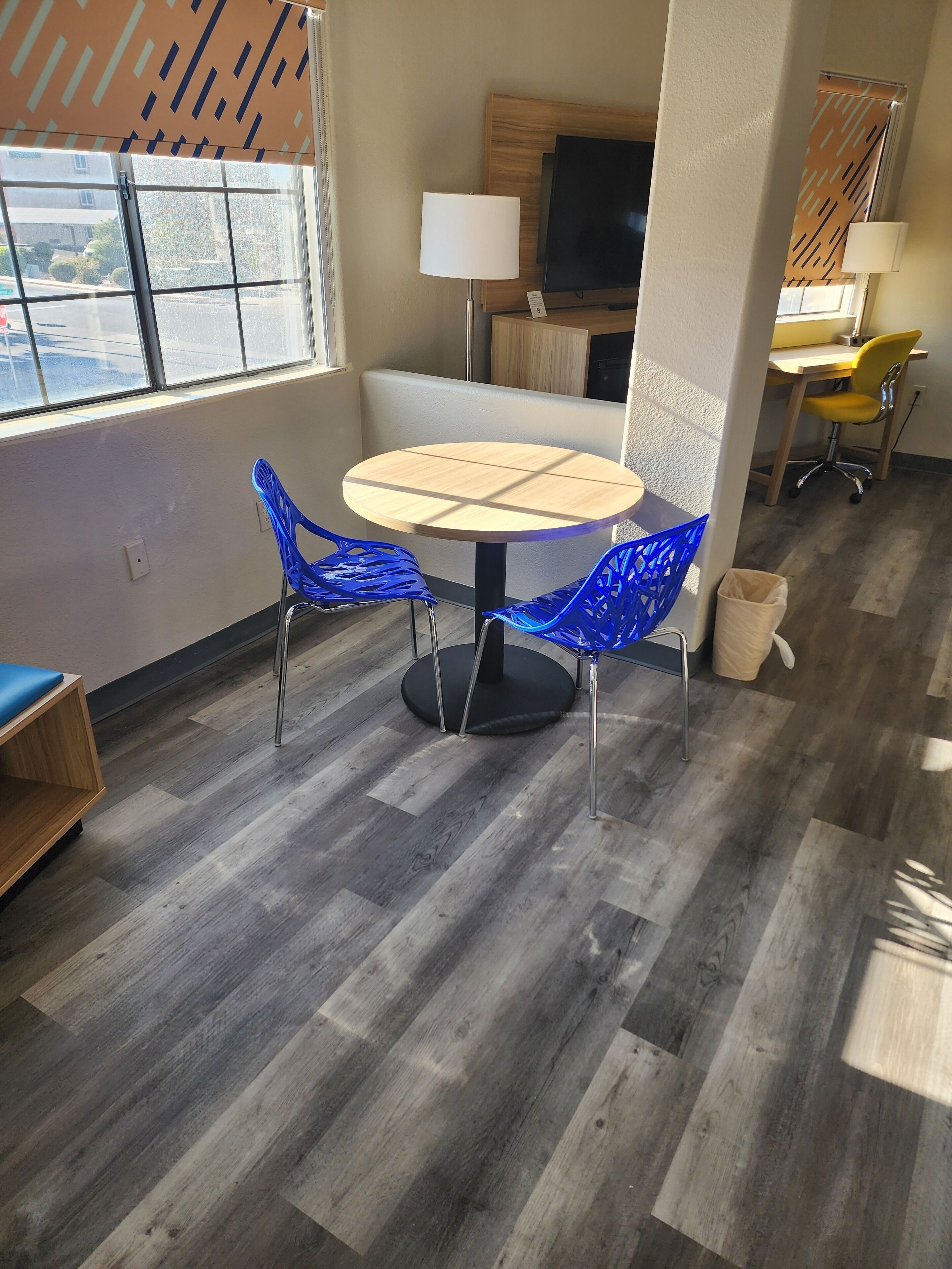 A modern room with a round table, two blue chairs, a TV, and a wooden desk with a chair.
