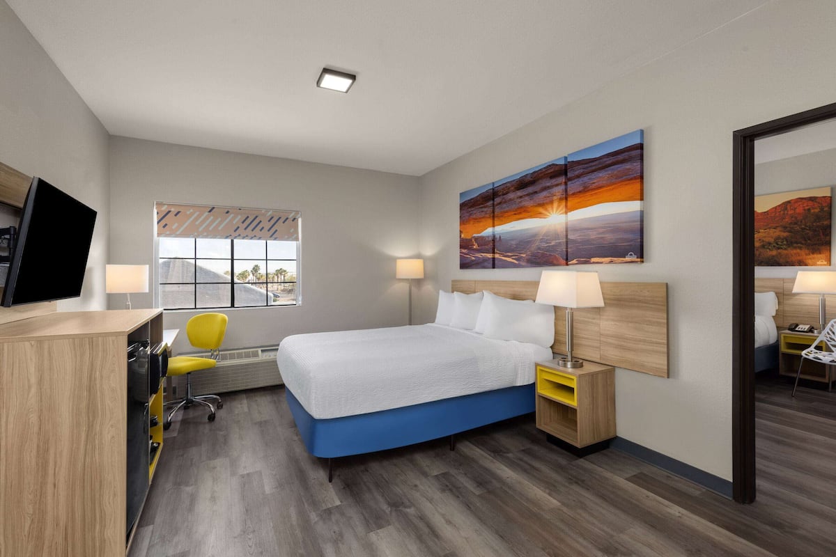 Una habitación de hotel moderna con una cama grande, un escritorio con una silla, un televisor y una ventana con persianas.