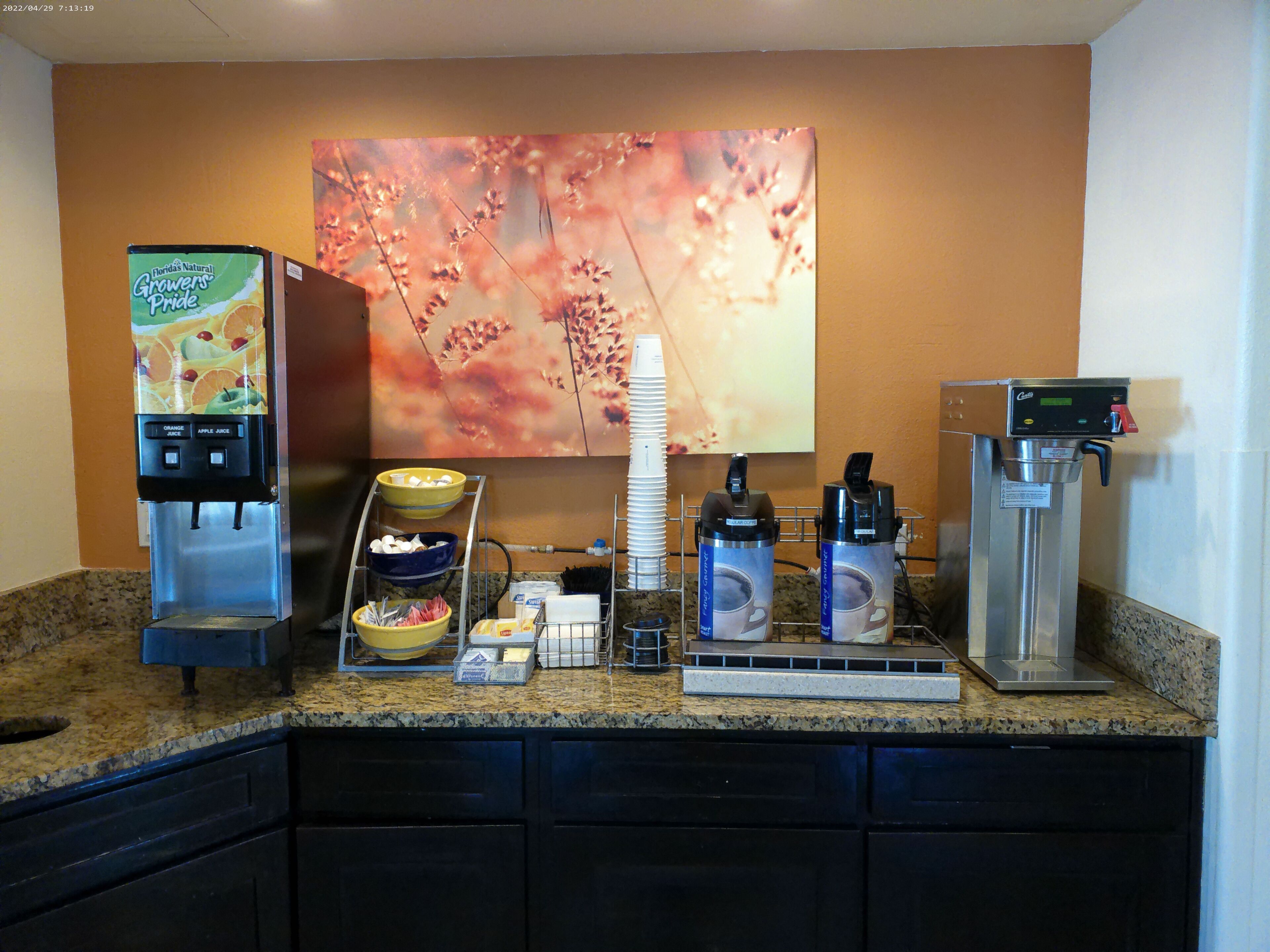 A self-service beverage station with a coffee machine, a juice dispenser, and a water dispenser.