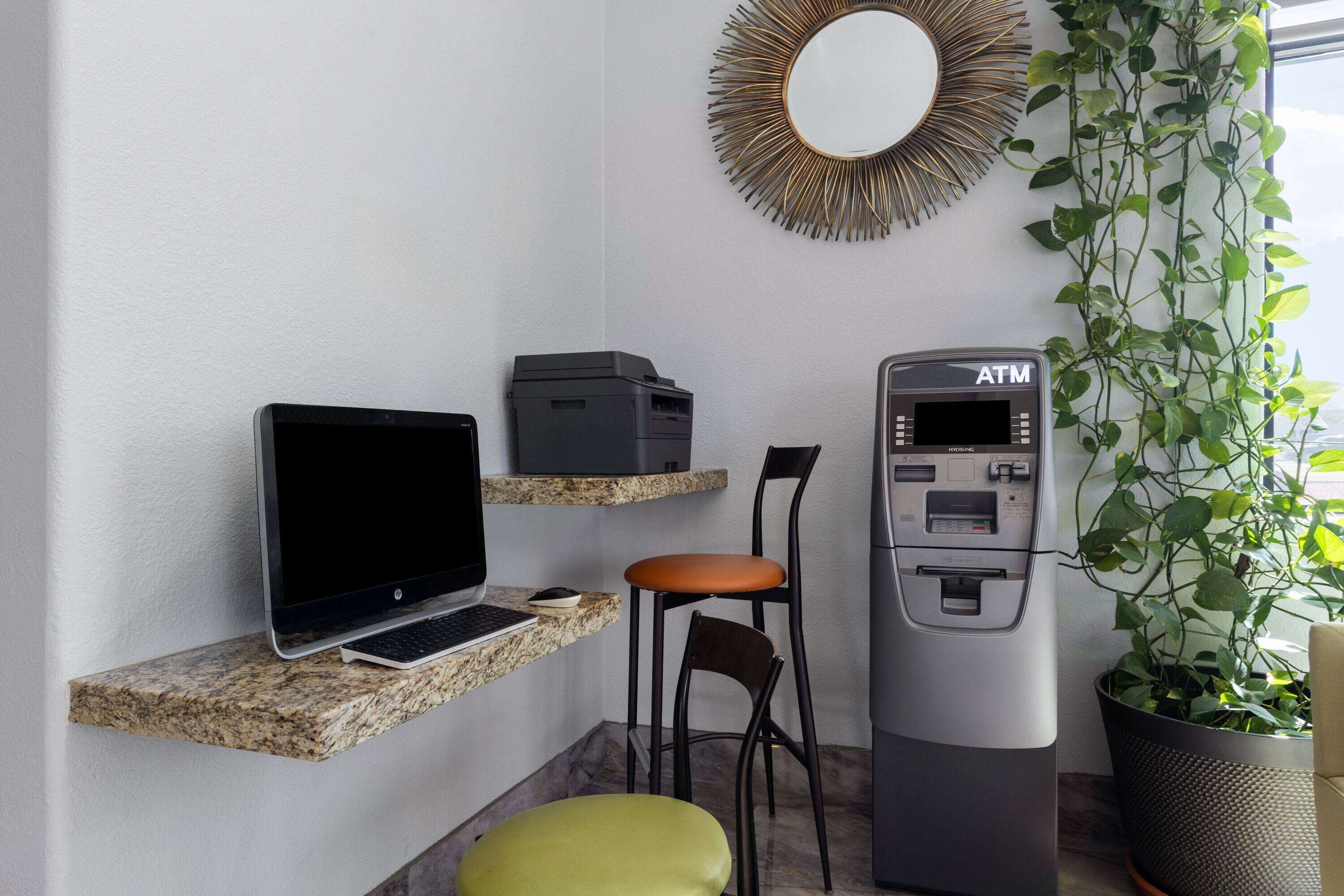 A workspace with a laptop, printer, ATM, and a chair.