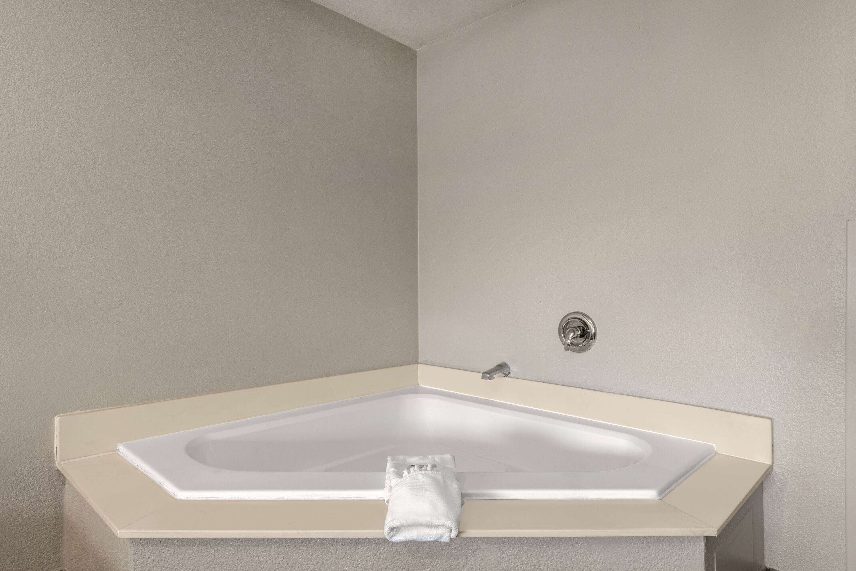 A corner bathtub with a beige frame and a white towel on it.