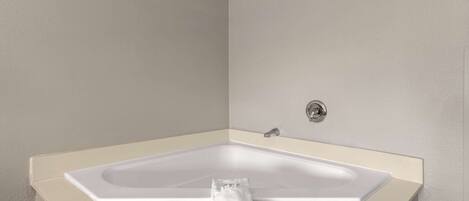 A corner bathtub with a beige frame and a white towel on it.