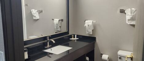 A bathroom with a dark wood vanity, a white sink, a large mirror, and a toilet.
