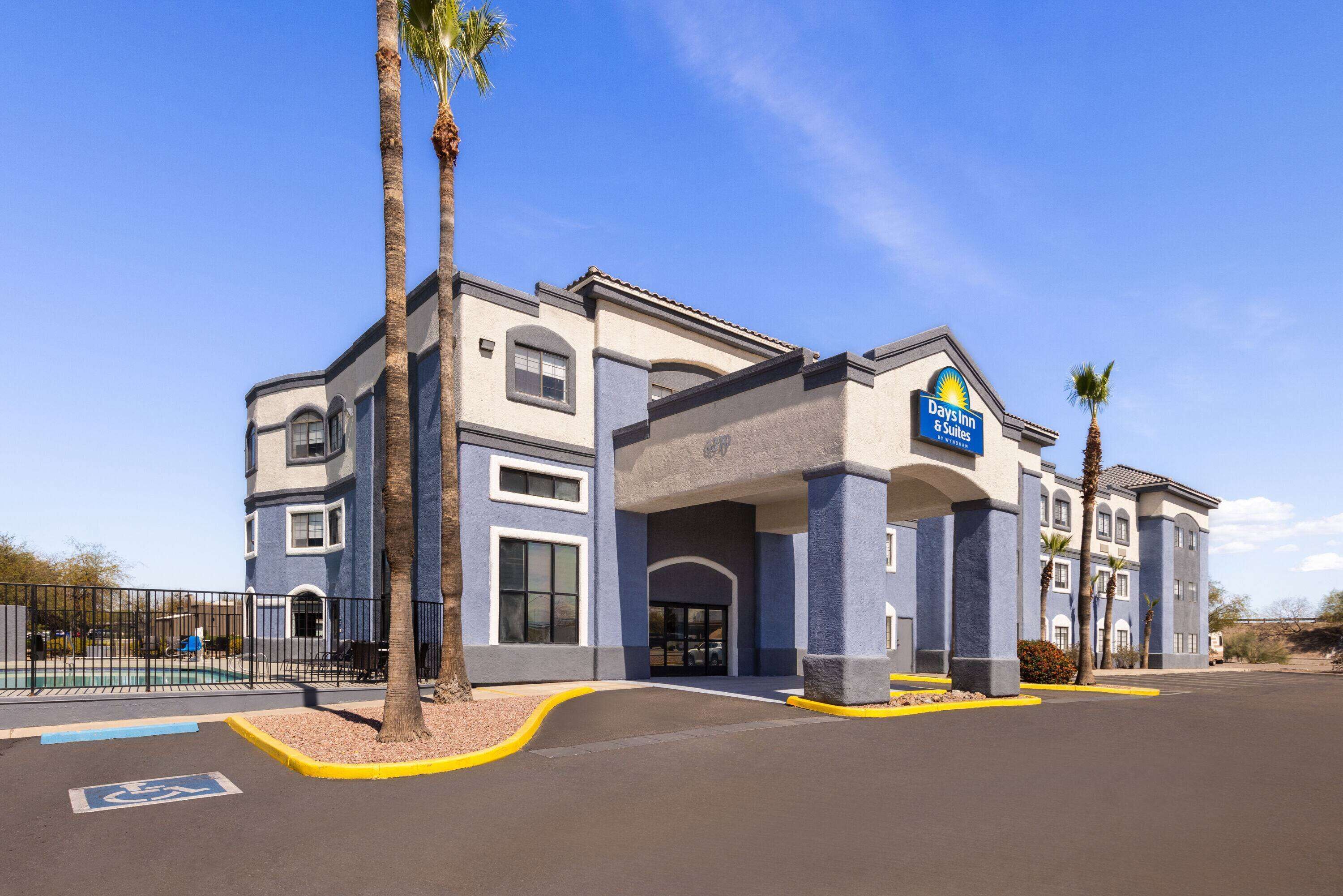 A Days Inn & Suites hotel with a modern design, featuring a large parking lot and a clear blue sky.