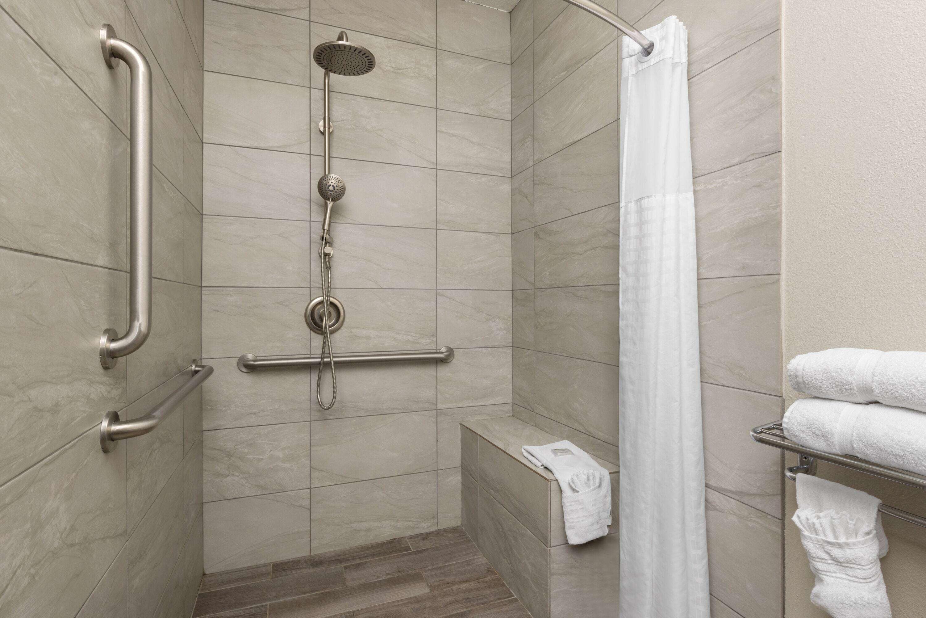 Une douche équipée d’un pommeau de douche à main, de barres d’appui et d’un porte-serviettes avec des serviettes.