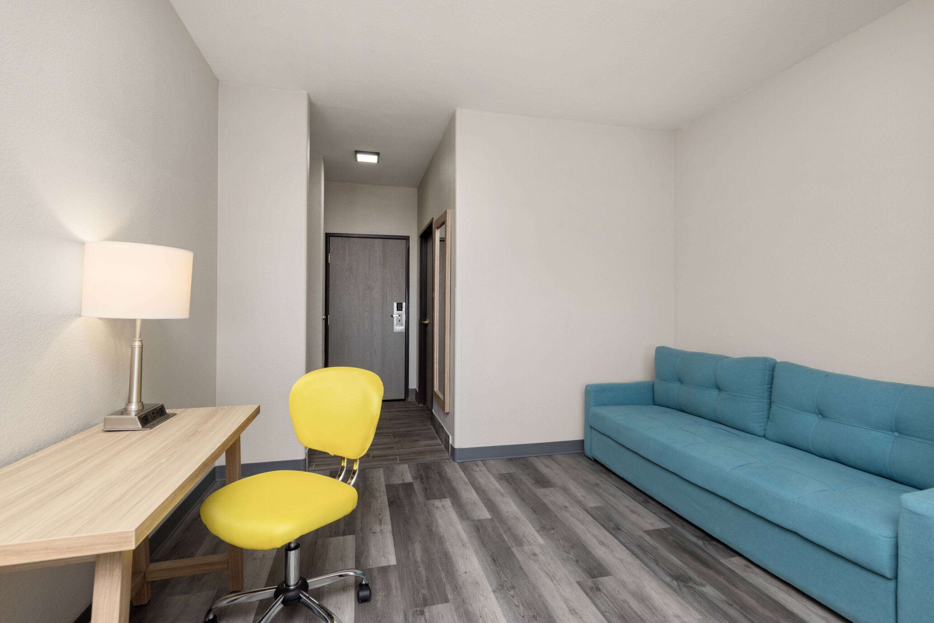 A small, modern room with a wooden desk, a yellow chair, a blue sofa, and a lamp.