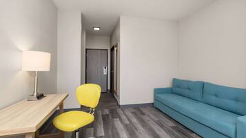 A small, modern room with a wooden desk, a yellow chair, a blue sofa, and a lamp.
