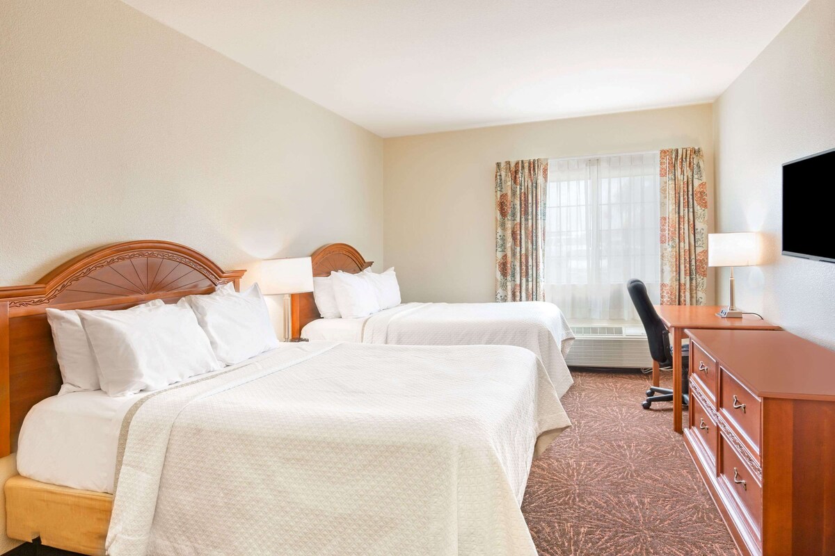 Une chambre d’hôtel avec deux lits, un bureau, une chaise et un téléviseur.