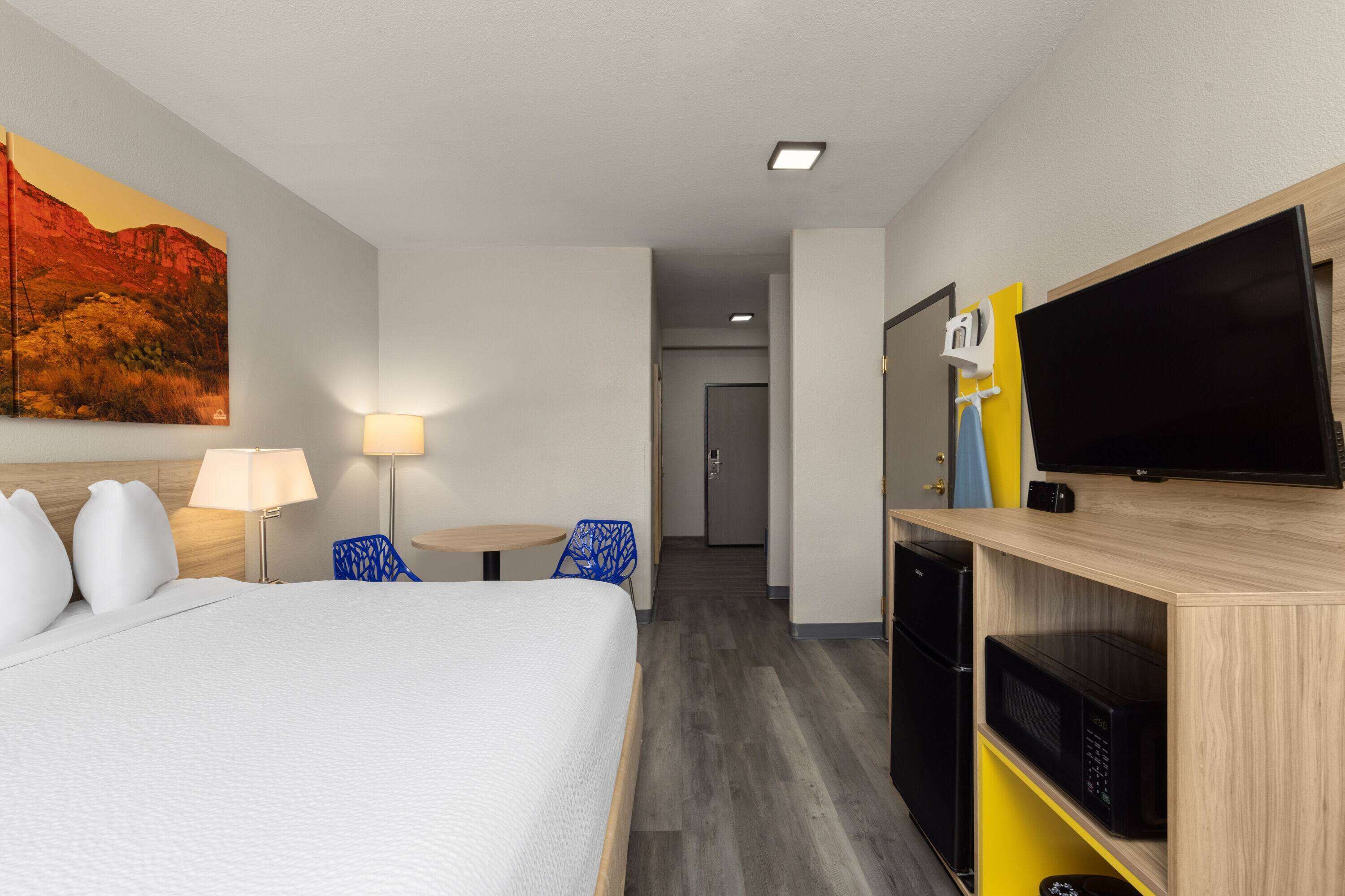Una habitación de hotel con cama, escritorio, silla, televisor y microondas.