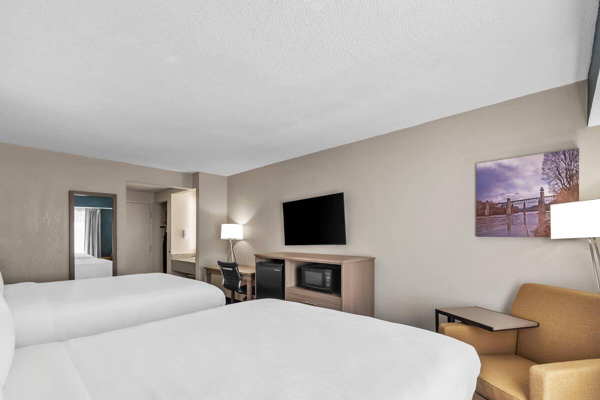 A hotel room with two beds, a desk with a computer, a TV, and a small table.