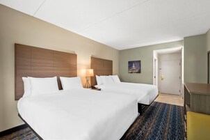 A hotel room with two beds, a desk, a lamp, and a door leading to another room.
