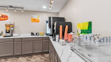 A breakfast bar with a coffee machine, orange and white cups, and a green sign.