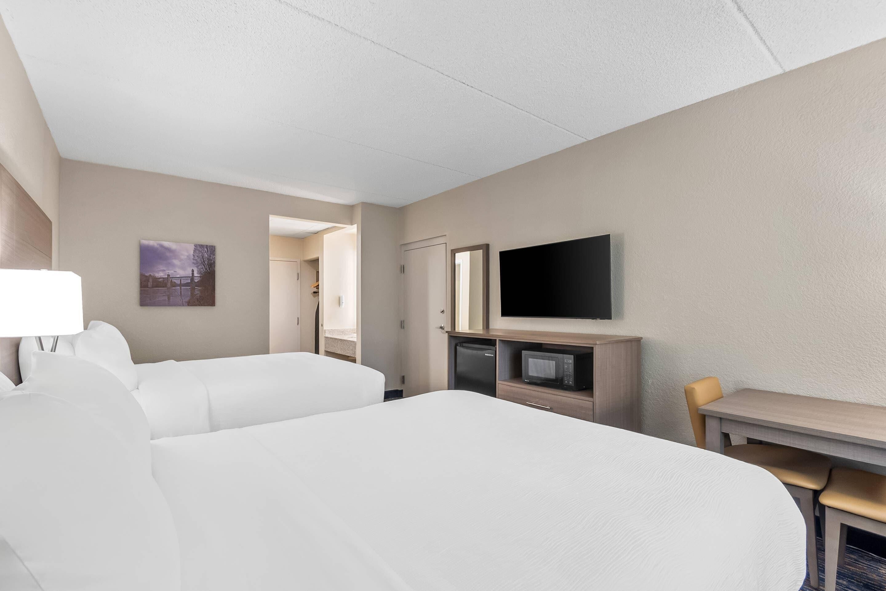A hotel room with two beds, a desk, a TV, and a microwave.