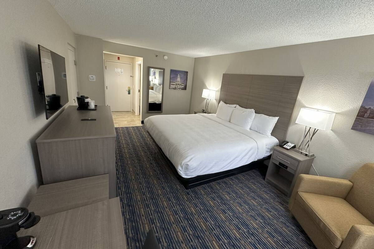 A hotel room with a large bed, a desk, a chair, a desk lamp, and a television.