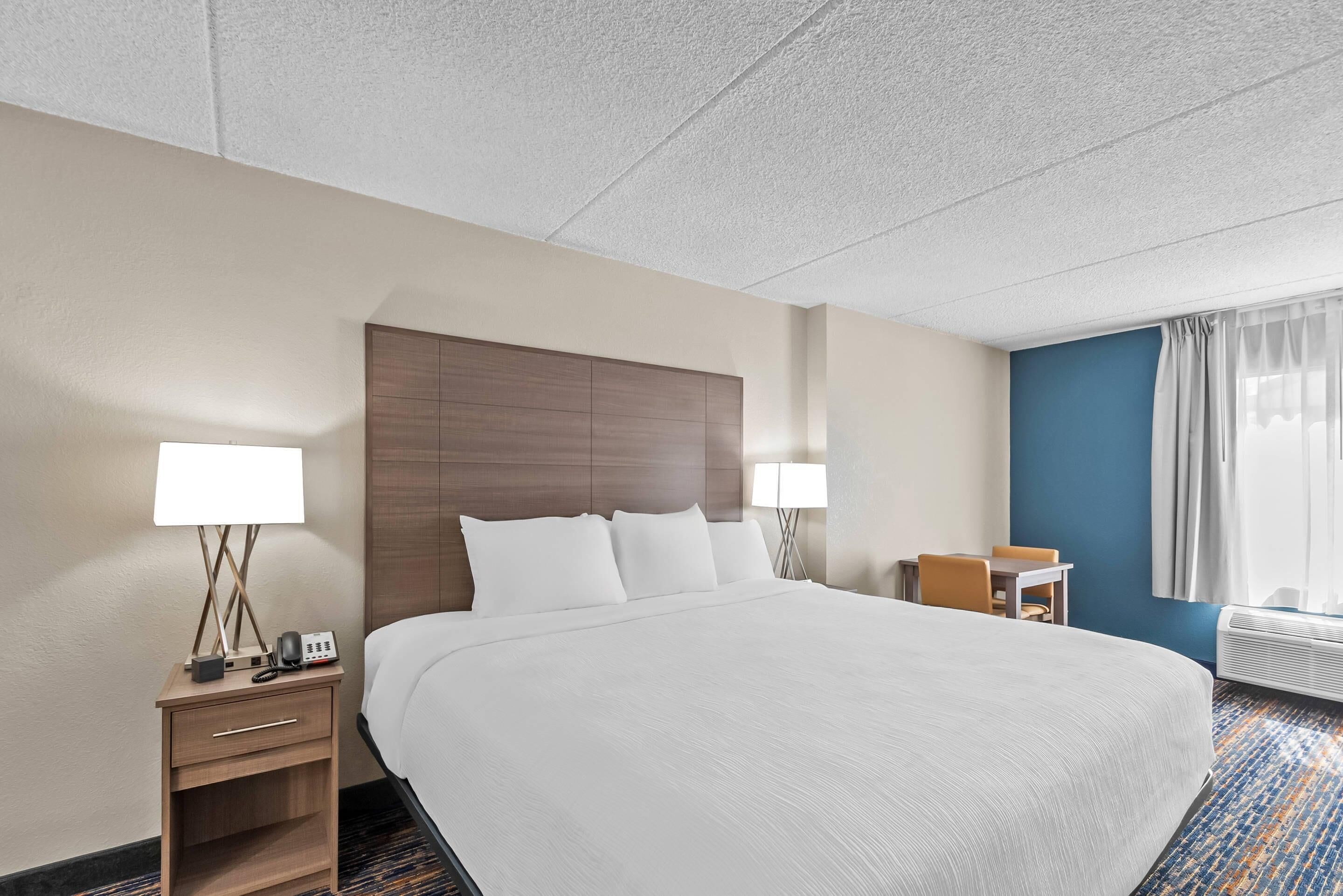 Una habitación de hotel con una cama grande, dos mesitas de noche con lámparas, un escritorio pequeño y una ventana con cortinas.