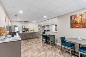 A modern kitchen area with a central island, a coffee station, and a dining area with blue chairs and a table.