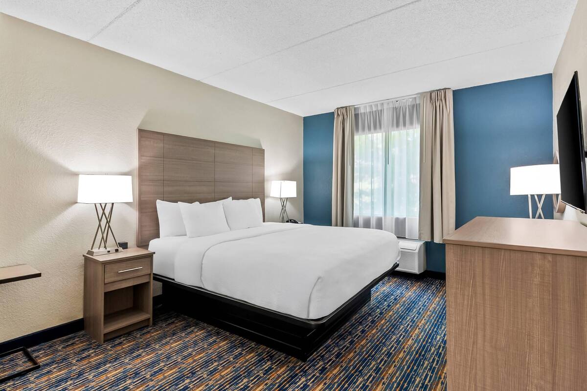 A hotel room with a large bed, a desk, a chair, a TV, and a window with curtains.