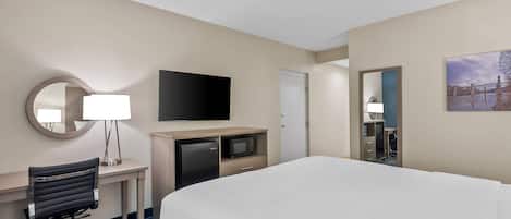 Quarto de hotel com cama, escrivaninha, cadeira, televisão e espelho.