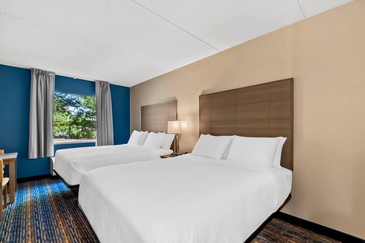A hotel room with two beds, a desk, and a window with curtains.