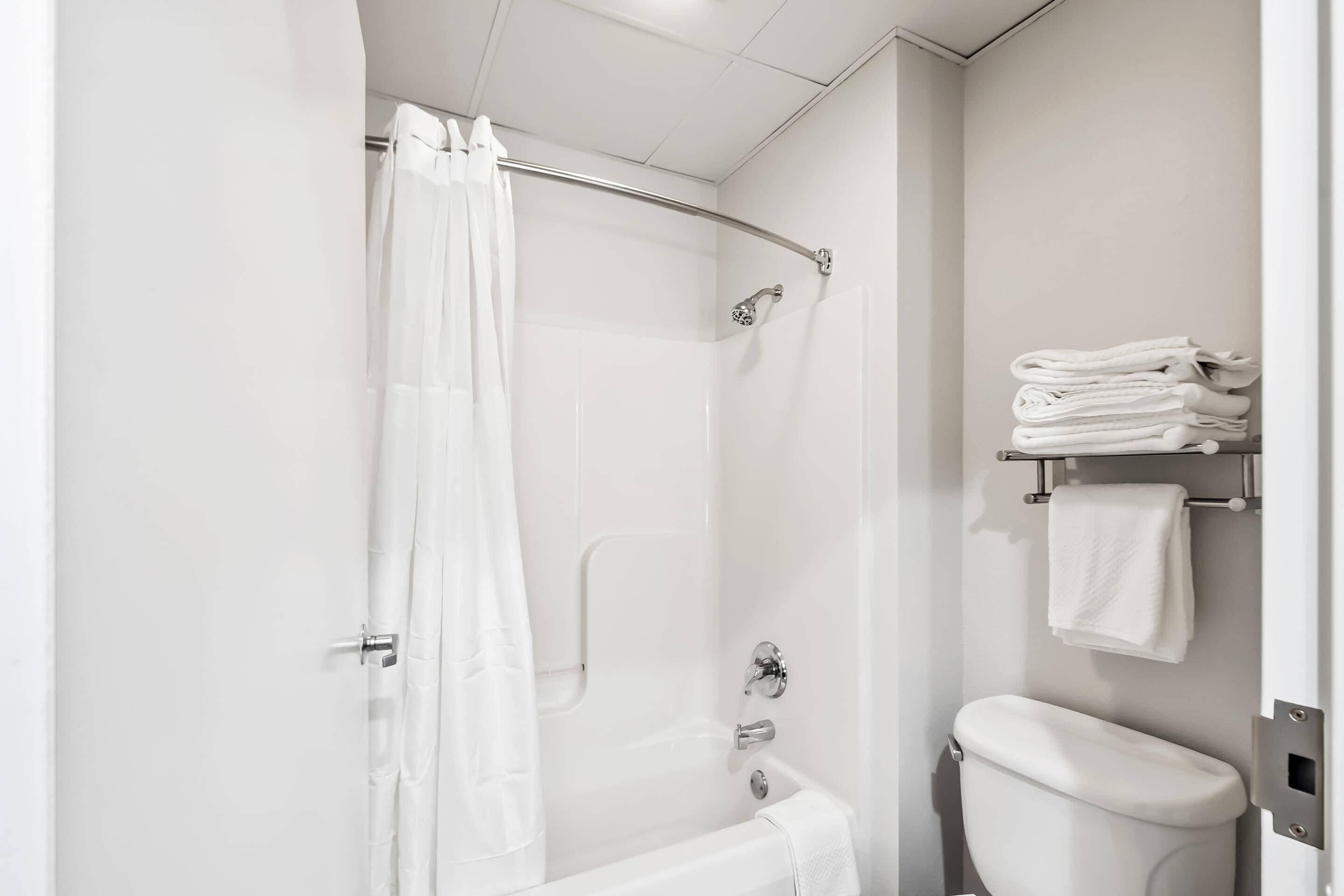 A modern bathroom with a glass-enclosed shower, a white toilet, and a towel rack with folded towels.