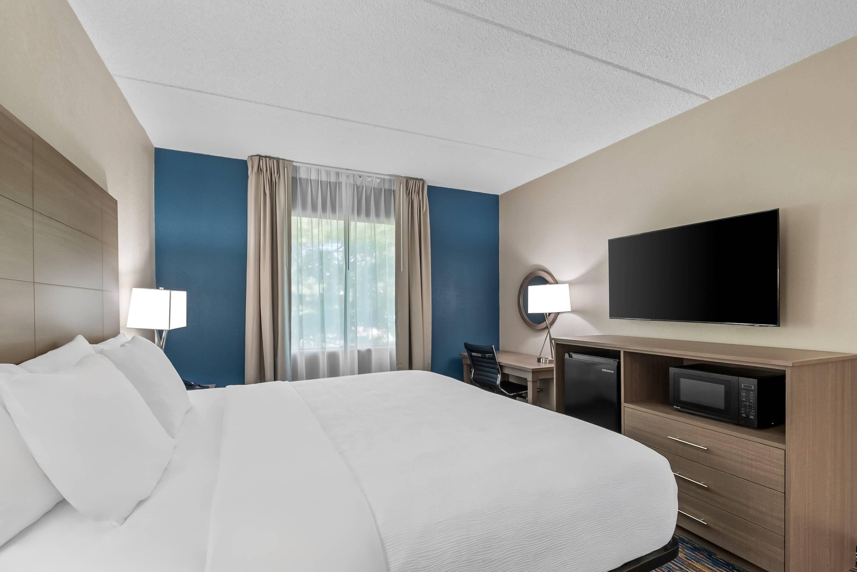 A hotel room with a large bed, a desk with a computer, a television, and a microwave.