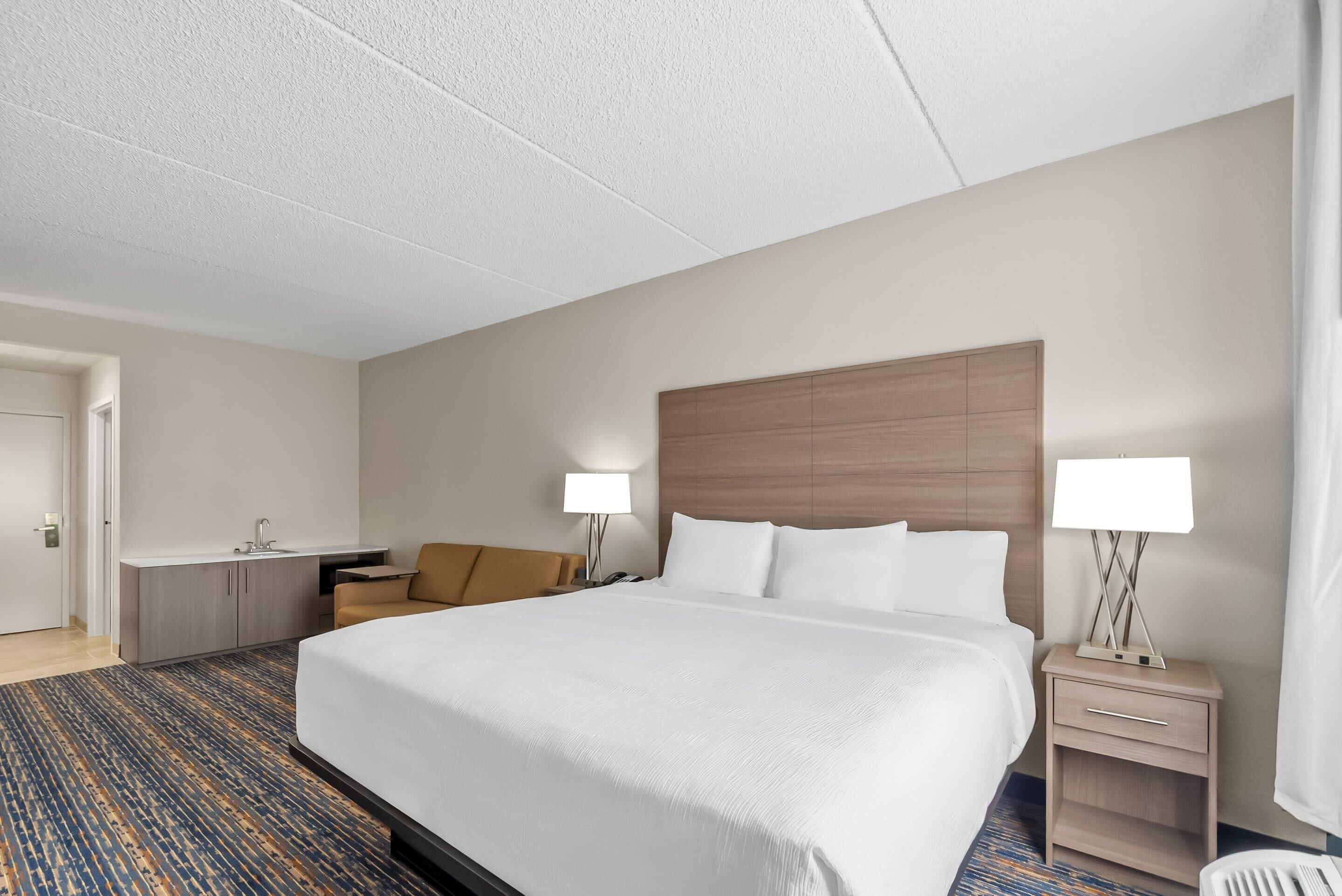 A hotel room with a large bed, a desk with a sink, a chair, and two bedside tables with lamps.