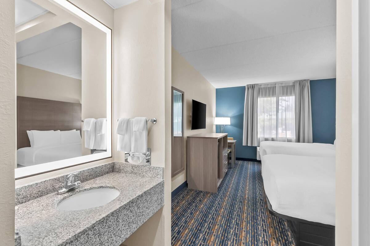 A hotel room with a granite sink, a bed, a TV, and a desk.