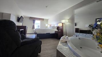 A hotel room with a bed, a large mirror, a bathtub, and a desk with a chair.