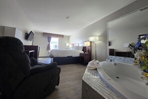 A hotel room with a bed, a large mirror, a bathtub, and a desk with a chair.