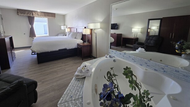 A hotel room with a bed, bedside tables, a large mirror, a bathtub, a sofa, and a television. - OYO Hampton South Carolina Hwy 278 (Hampton)