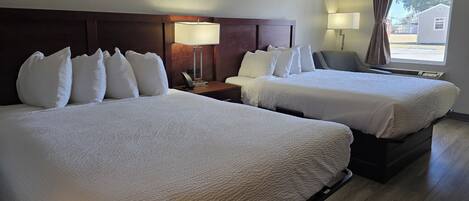 A hotel room with two beds, a nightstand with a lamp, a chair, and a window with curtains.