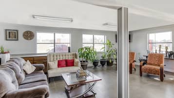 A spacious living room with a sofa, armchairs, and a coffee table. There are large windows and potted plants.