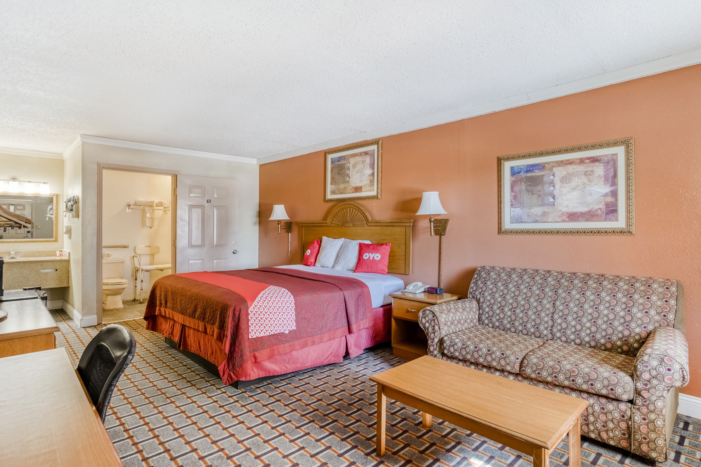 A hotel room with a bed, a sofa, a desk, and a chair. There is a bathroom with a toilet and a sink.