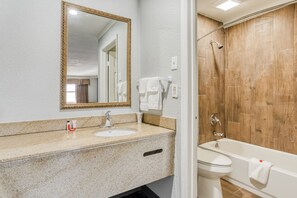 A bathroom with a granite countertop, a sink, a mirror, a shower, and a toilet.