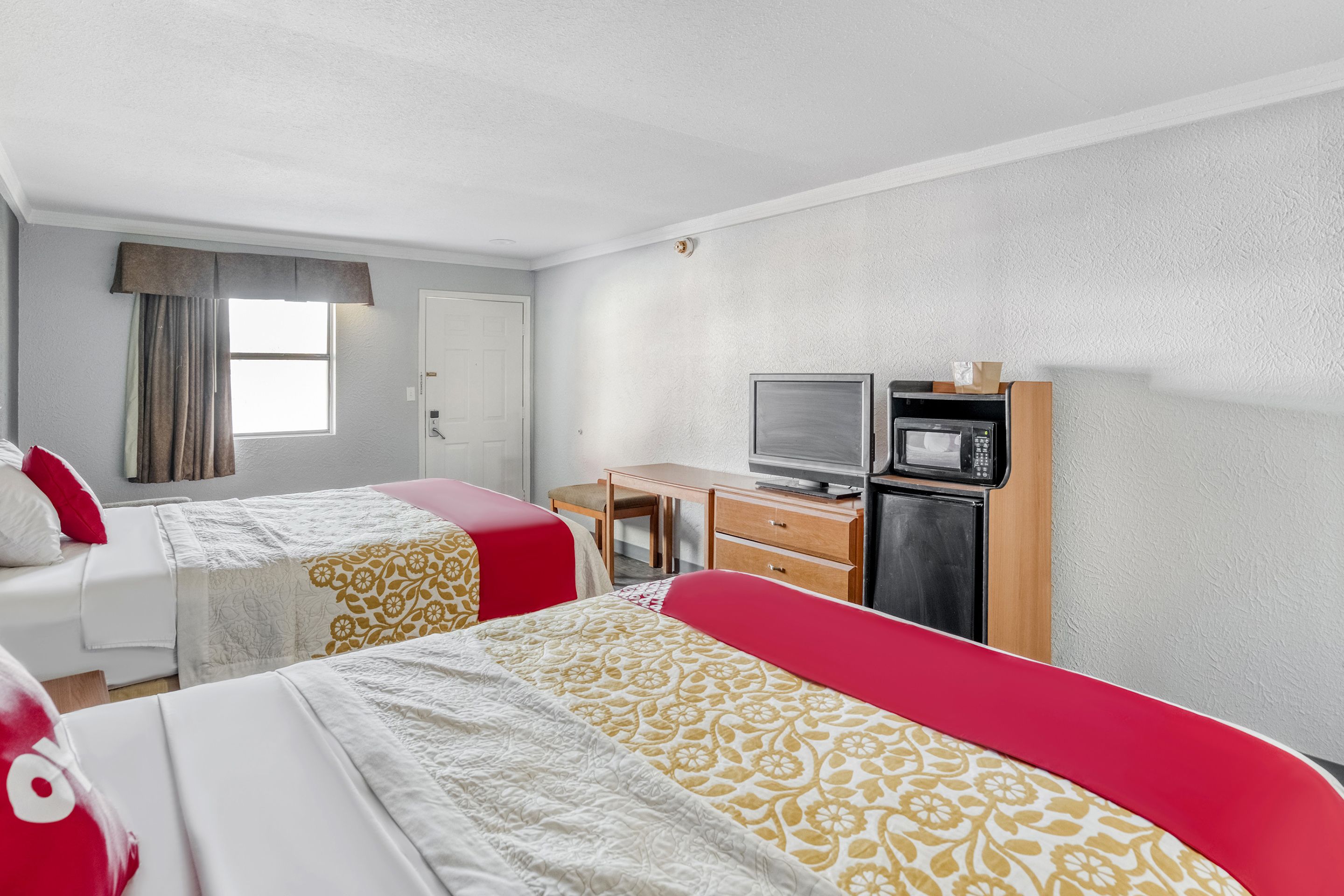 A hotel room with two beds, a desk, a television, and a microwave.
