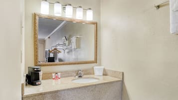 A bathroom with a large mirror, a sink, a coffee maker, and toiletries.