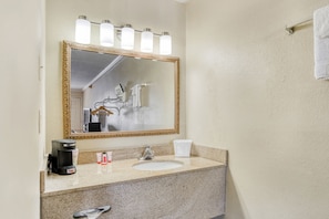 Un baño con un espejo grande, un lavabo, una cafetera y artículos de aseo.