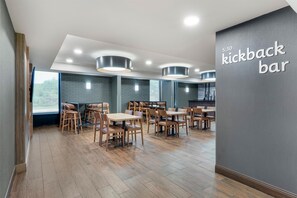 A modern dining area with wooden tables and chairs, recessed ceiling lights, and a sign reading 'kickback bar'. - Drury Inn & Suites Birmingham Grandview (Birmingham)