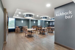 Un comedor moderno con mesas y sillas de madera, luces empotradas en el techo y un letrero que dice 'kickback bar'.
