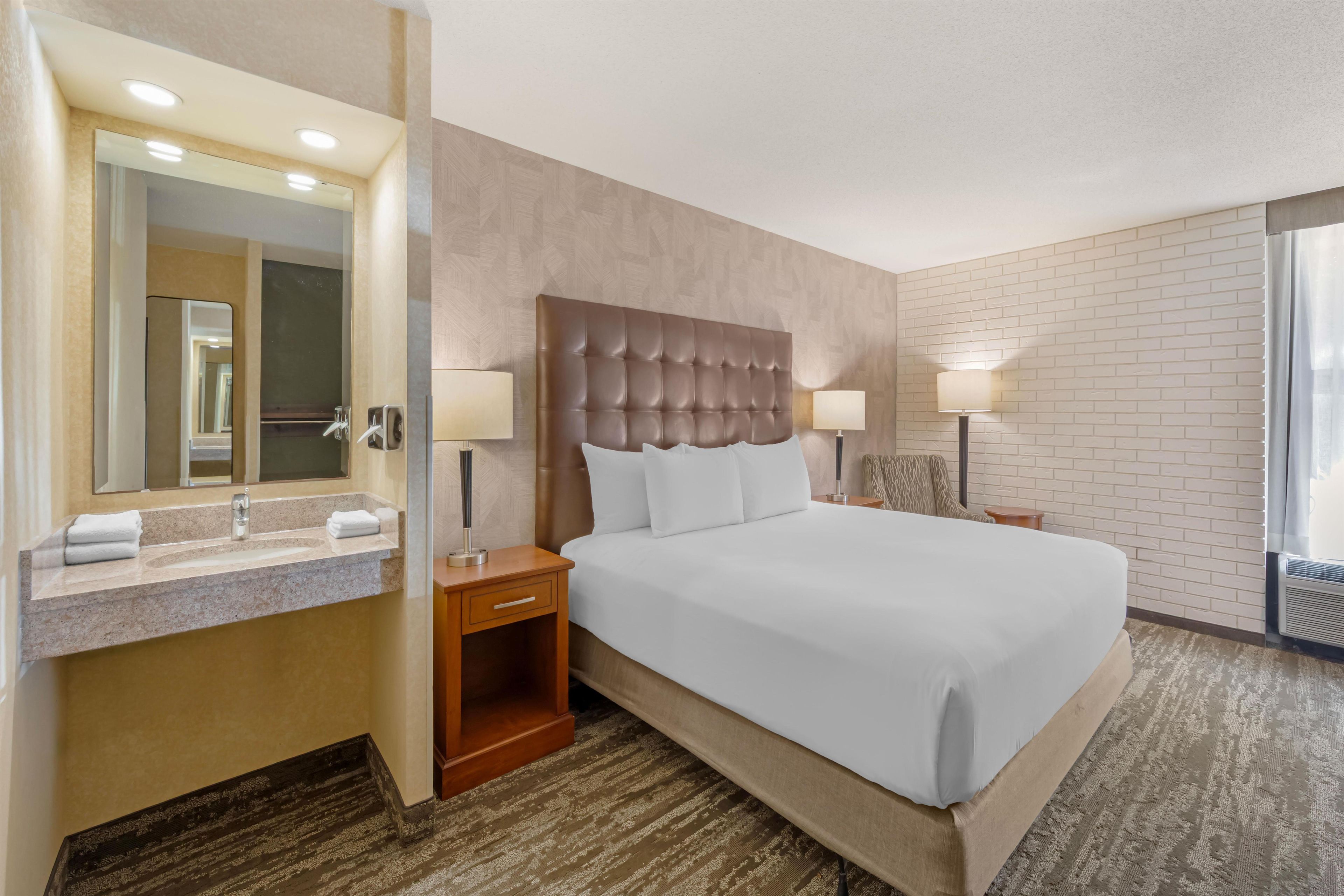 A hotel room with a large bed, a bathroom with a mirror, and a window.