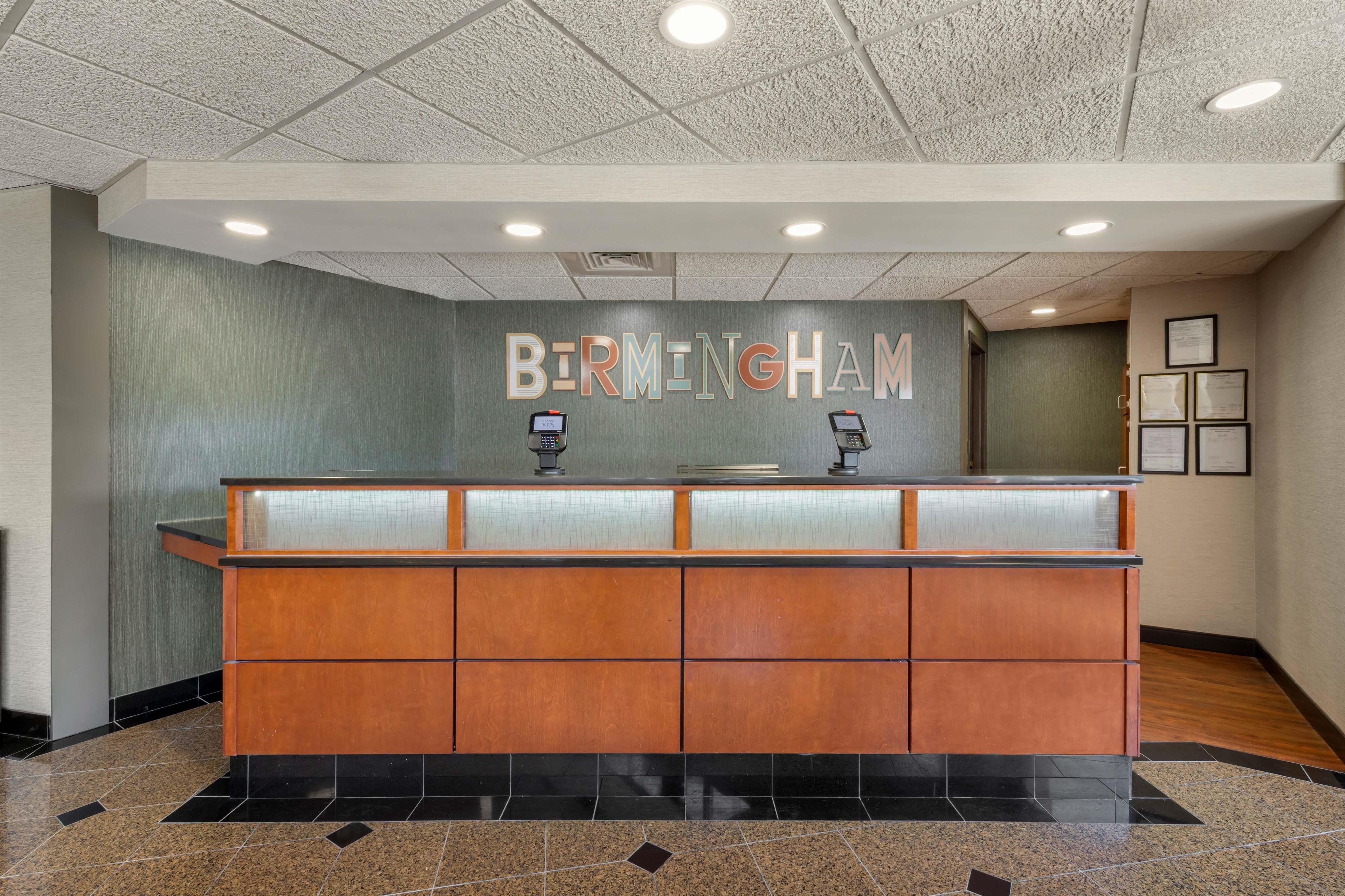 A reception desk with a 'BIRMINGHAM' sign above it, a glass partition, and framed certificates on the wall.